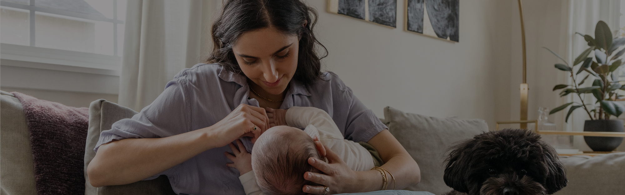Woman holding a baby in a living room with a dog and plants.