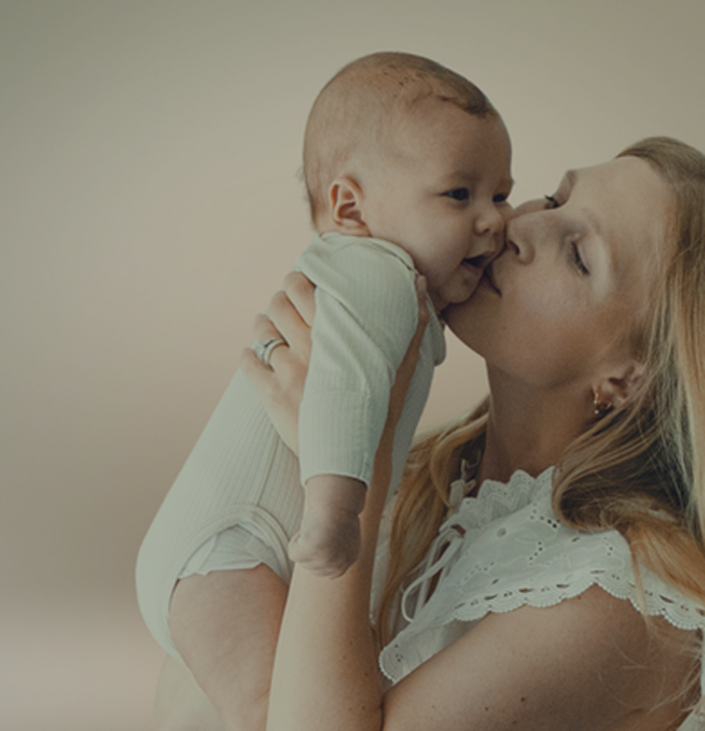 Woman kissing a baby on the nose against a plain background