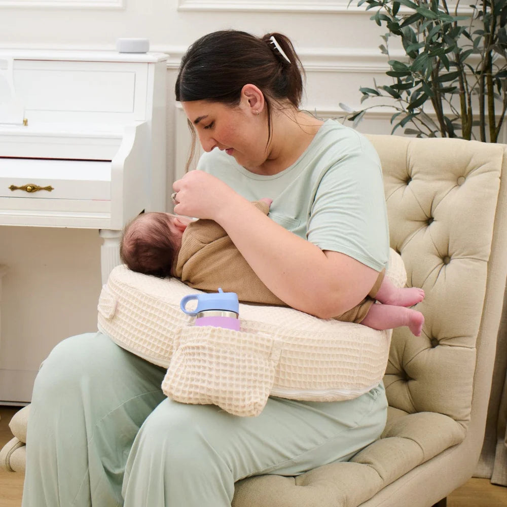 Woman breastfeeding a baby using a nursing pillow in a cozy living room.