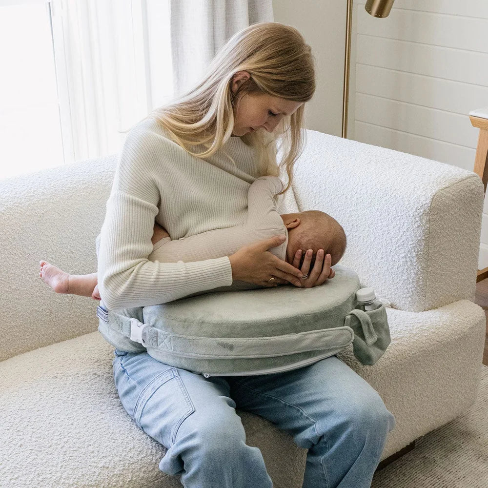 Woman breastfeeding a baby using a nursing pillow in a cozy room.
